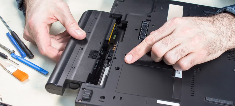 Laptop service. Removal of the battery by a service technician. Tools lie on the table next to it.